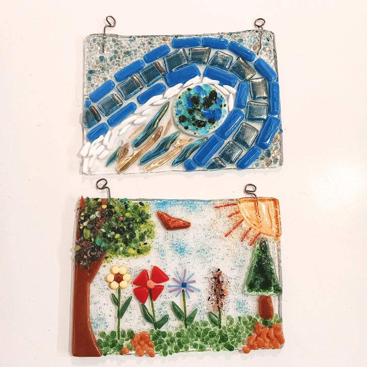 FG_Suncatcher_Rectangle_720x720 Two fused glass art pieces: one with abstract swirling patterns and another depicting a natural landscape with trees, flowers, and a sun.
