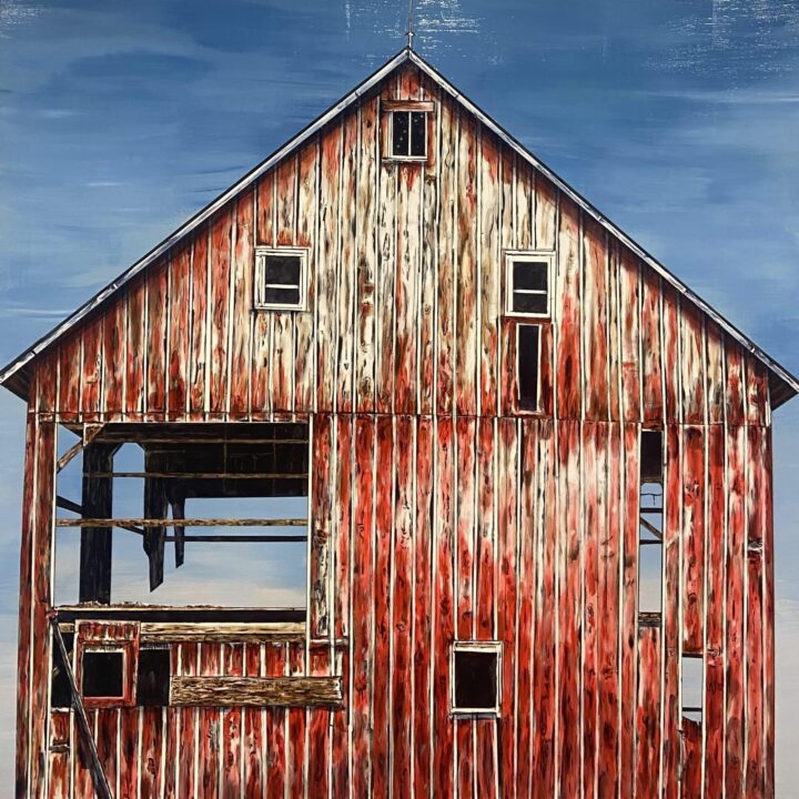Old red barn with a weathered facade and missing window panes against a blue sky.