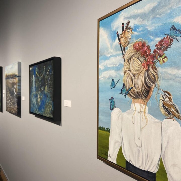 A painting of a woman with an updo featuring flowers and birds, displayed in an art gallery.